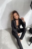 Rozpięta czarna marynarka damska z zapięciem na guzik i czarną koronką przy nadgarstkach, założona do czarnych legginsów z wysokim stanem